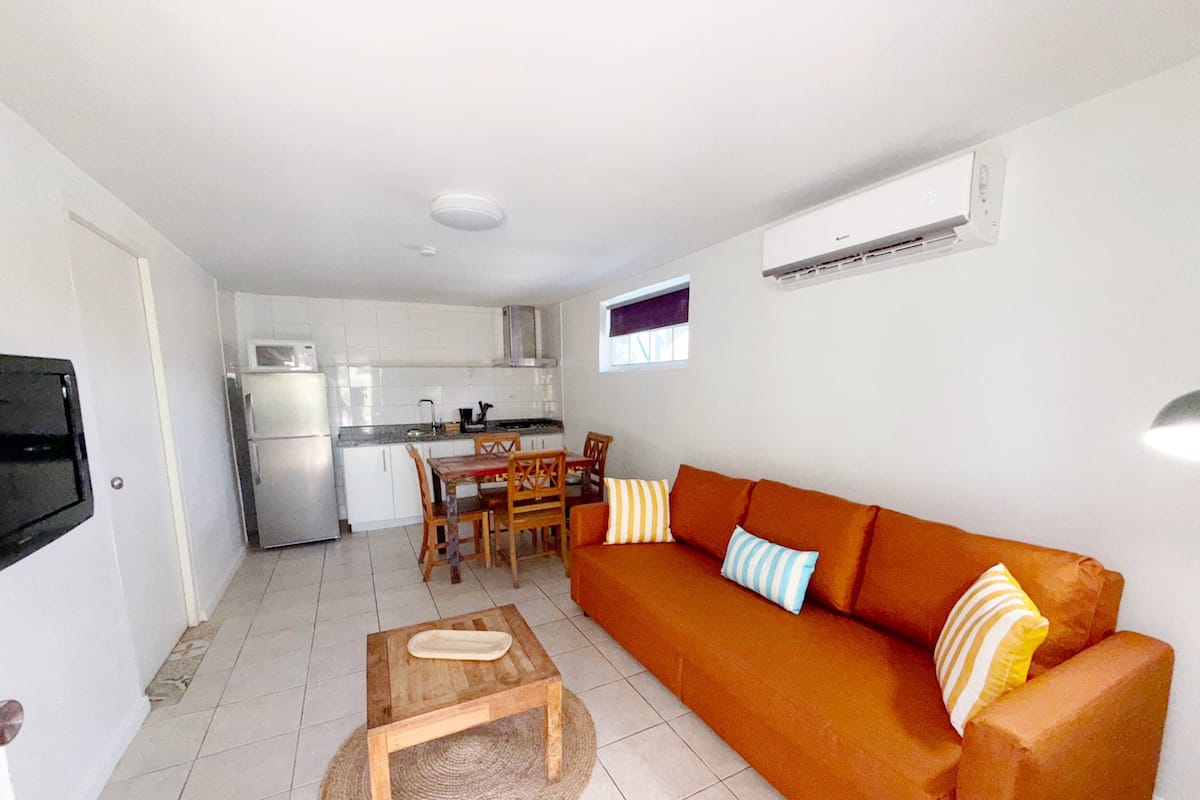 Un espacio habitable compacto con kitchenette, un sofá, una mesa de centro y un televisor montado en la pared.