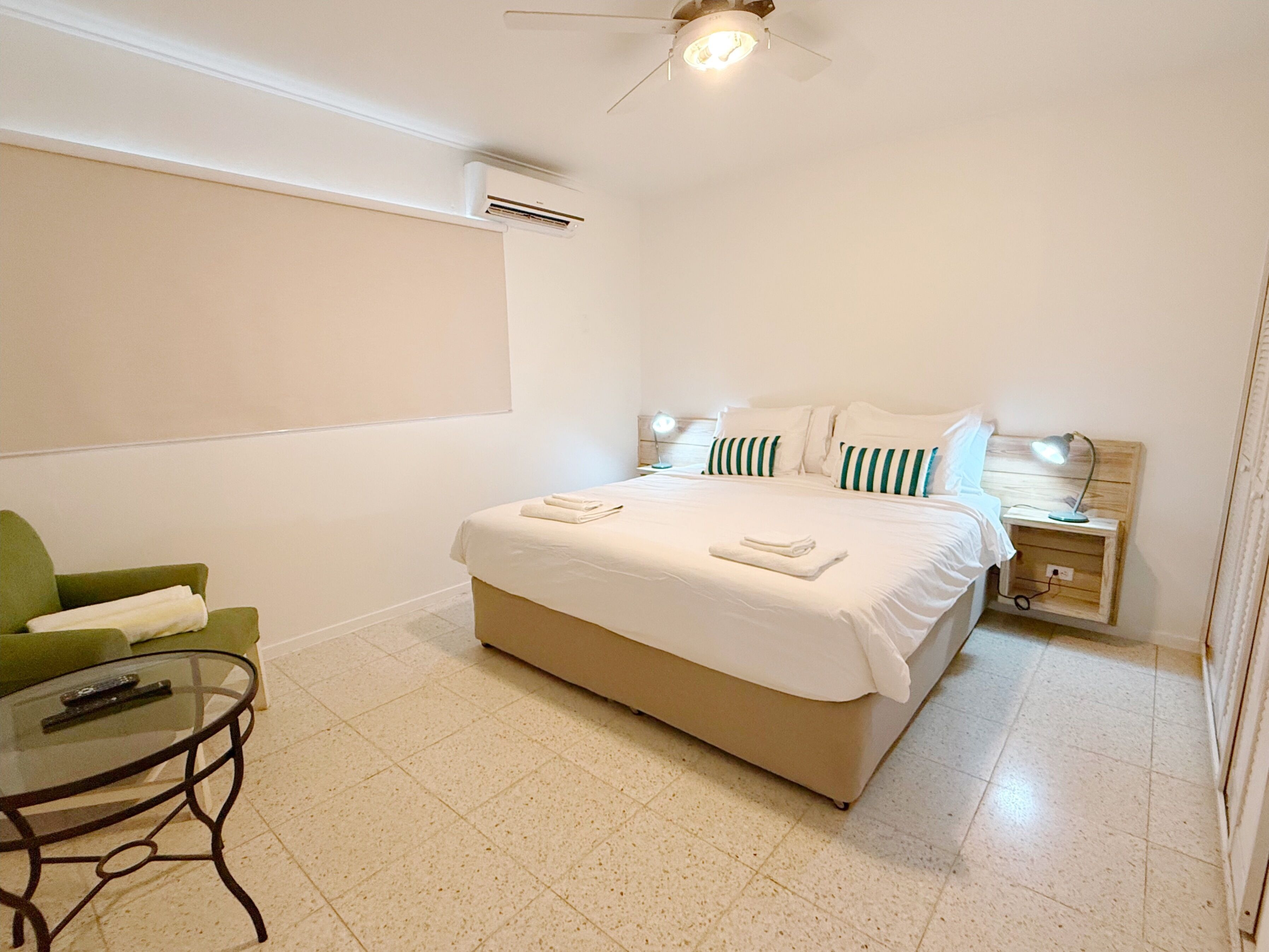 A bedroom with a bed, a nightstand, a green chair, and a glass table.