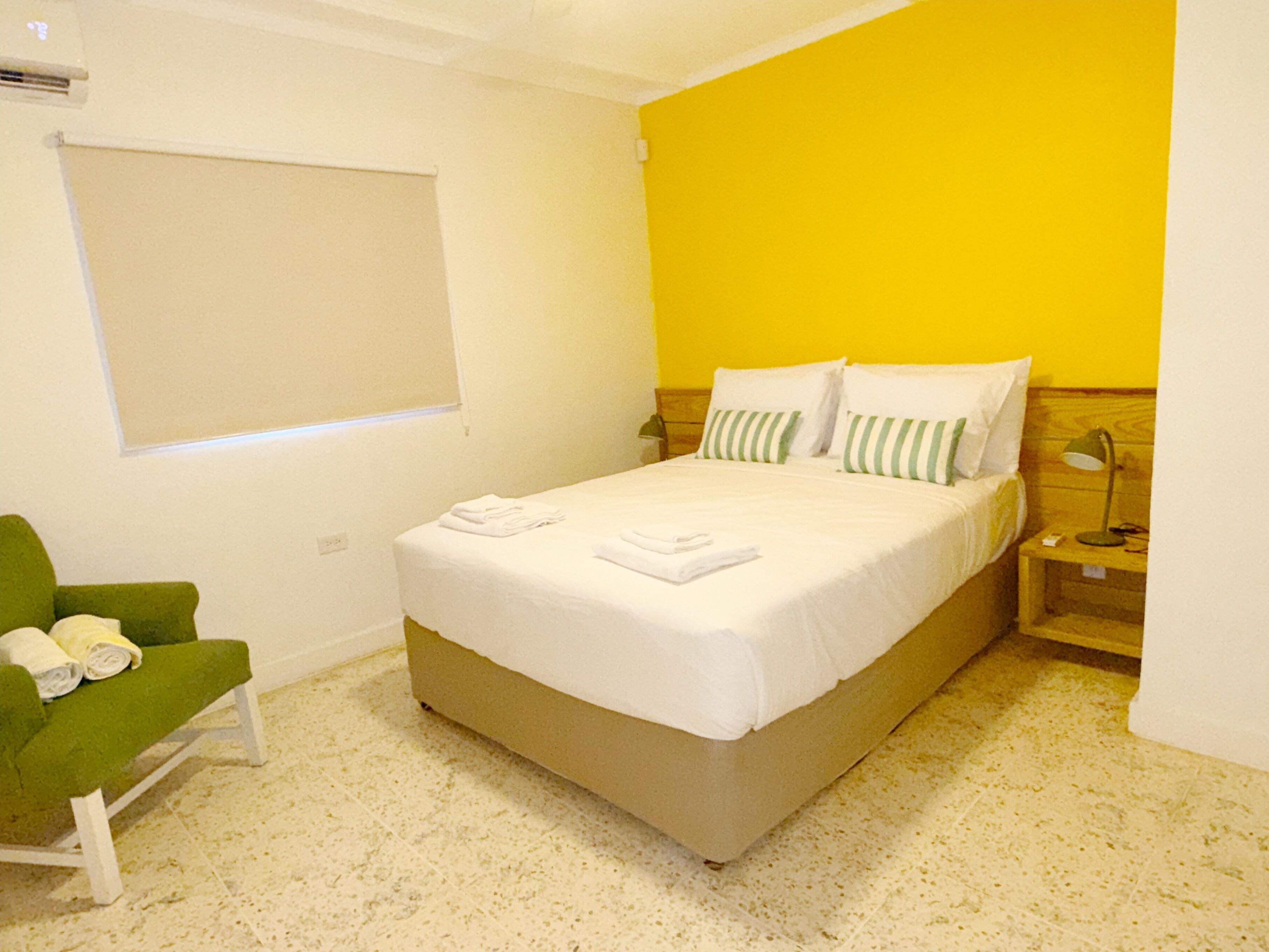 Un dormitorio con cama, una silla verde, una mesita de noche y una ventana.