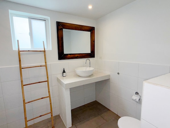 A bathroom with a white sink, a wooden-framed mirror, a toilet, and a wooden ladder leaning against the wall. - Aruba Palms Escape Suites (Noord)