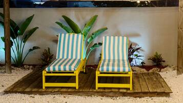 Dos sillones a rayas en una terraza de madera con suelo blanco texturizado, rodeados de plantas tropicales.