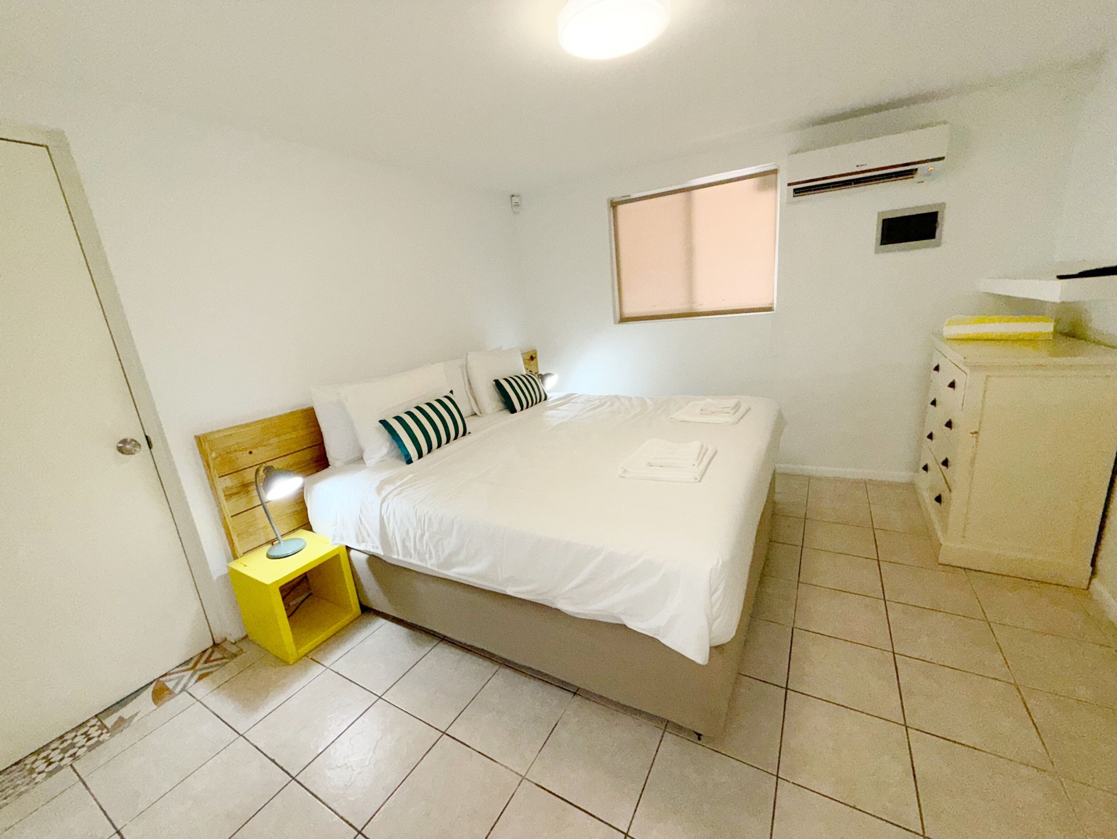 Une chambre à coucher comprenant un lit, une table de chevet, une fenêtre et un appareil de climatisation.