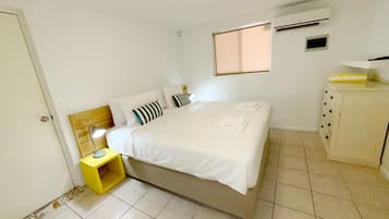 Une chambre à coucher comprenant un lit, une table de chevet, une fenêtre et un appareil de climatisation.