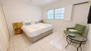 Un dormitorio con una cama, una silla verde, una mesita de cristal y un ventilador de techo.