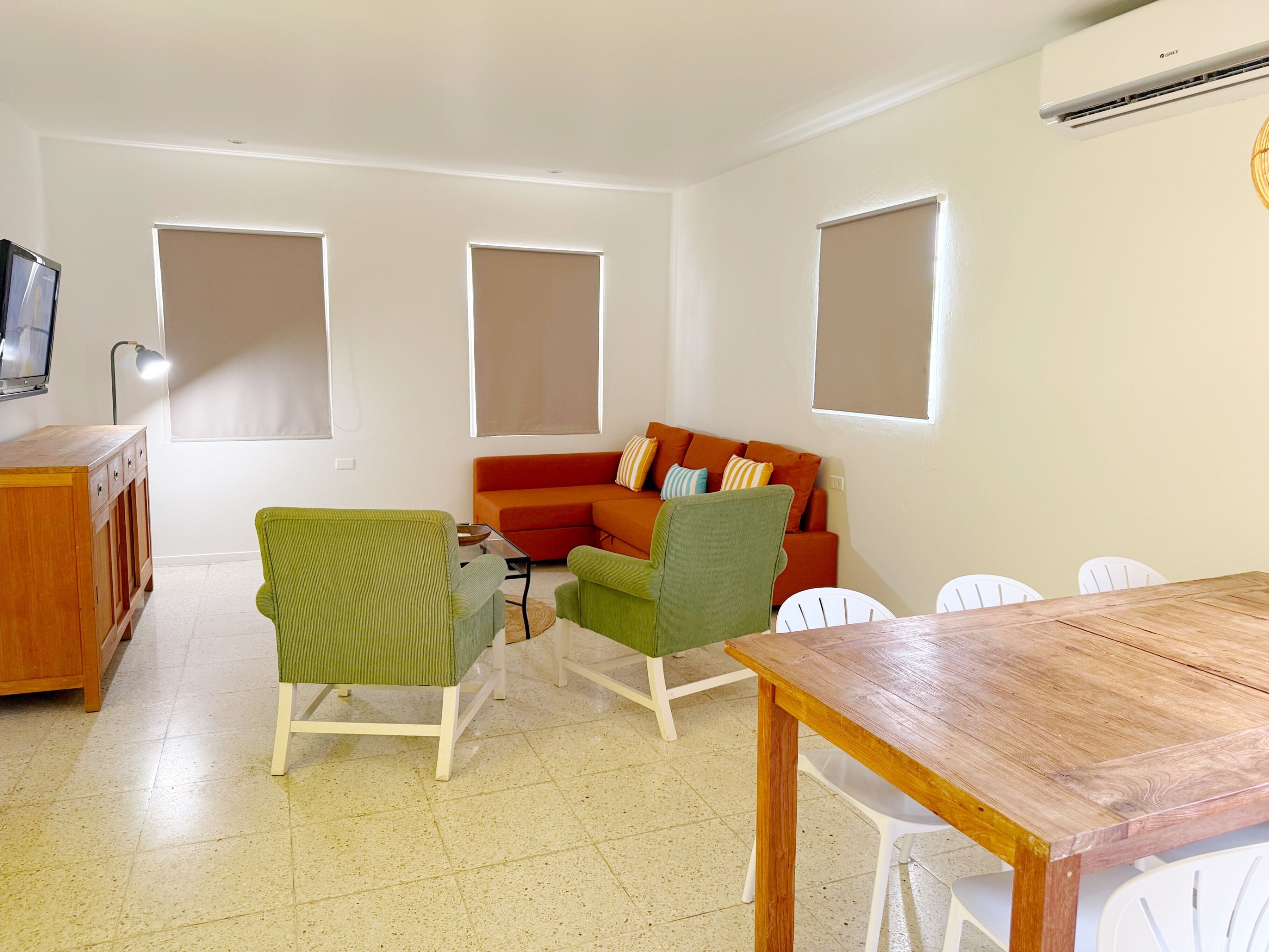 A living room with a wooden table, green chairs, a red sofa, and a TV on a wooden cabinet.