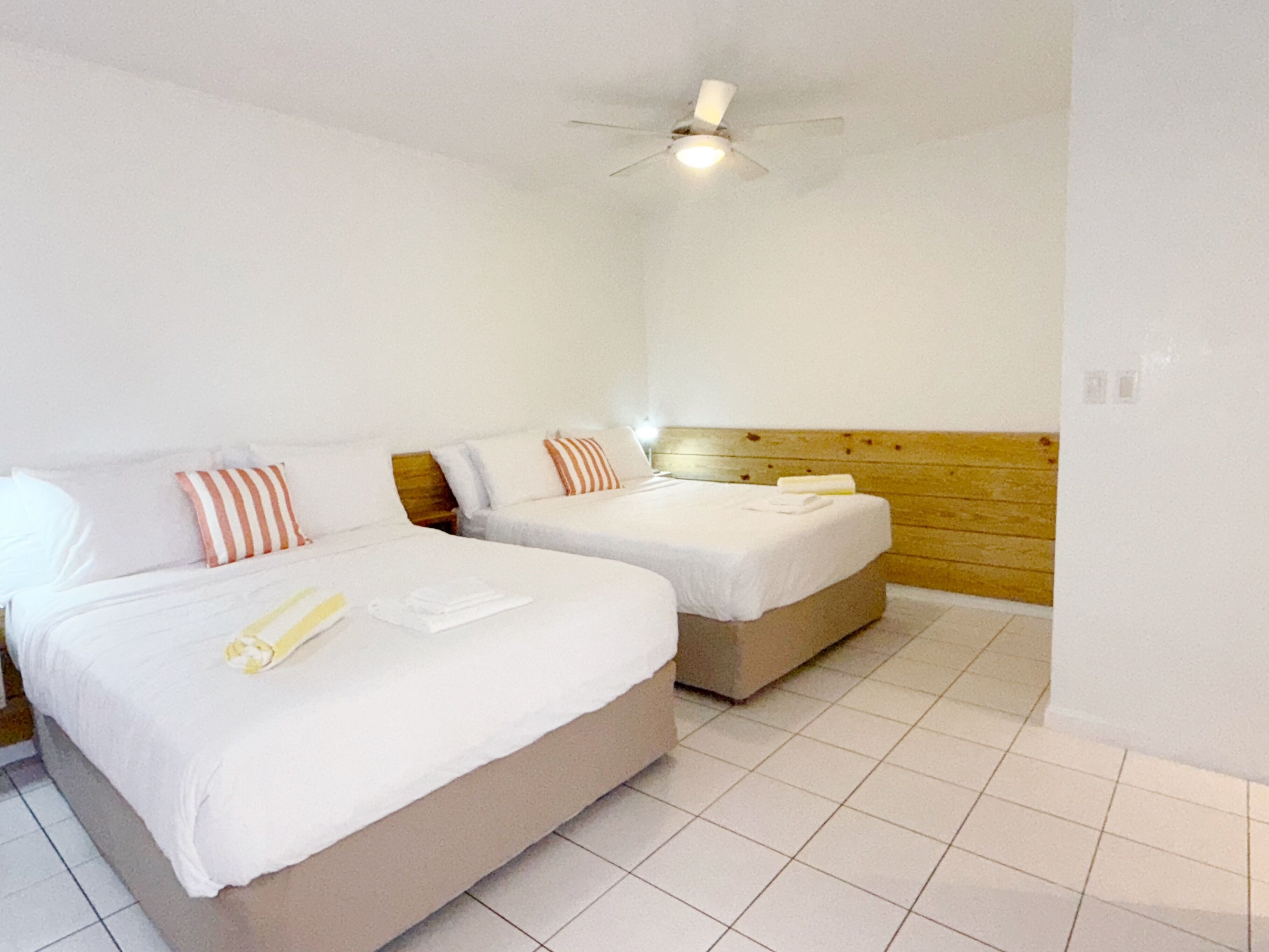A hotel room with two beds, white bedding, striped pillows, a wooden headboard, and a ceiling fan.