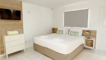 A bedroom with a bed, a TV mounted on the wall, a bedside table with a lamp, and a wooden headboard.