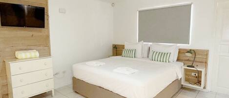 A bedroom with a bed, a TV mounted on the wall, a bedside table with a lamp, and a wooden headboard.
