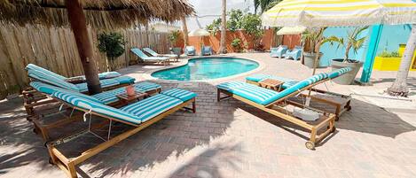 A pool area with lounge chairs and a thatched umbrella.