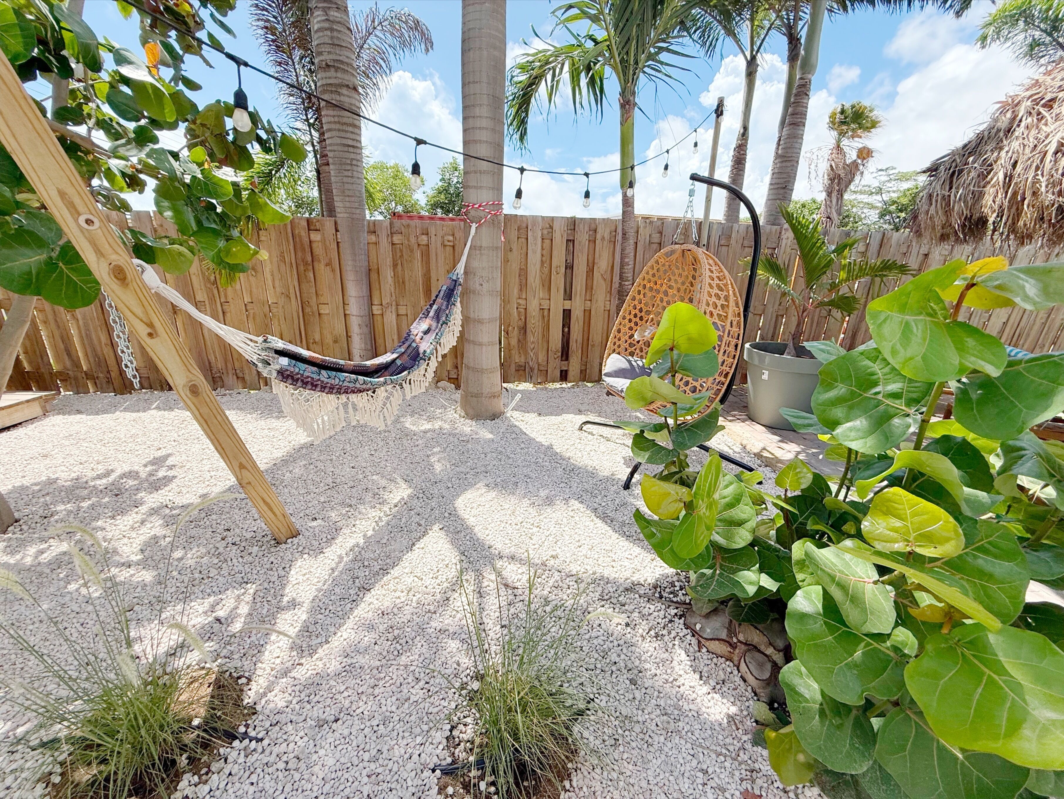 Una hamaca, un conjunto de columpios de madera y una cerca de madera en un jardín con suelo de grava.