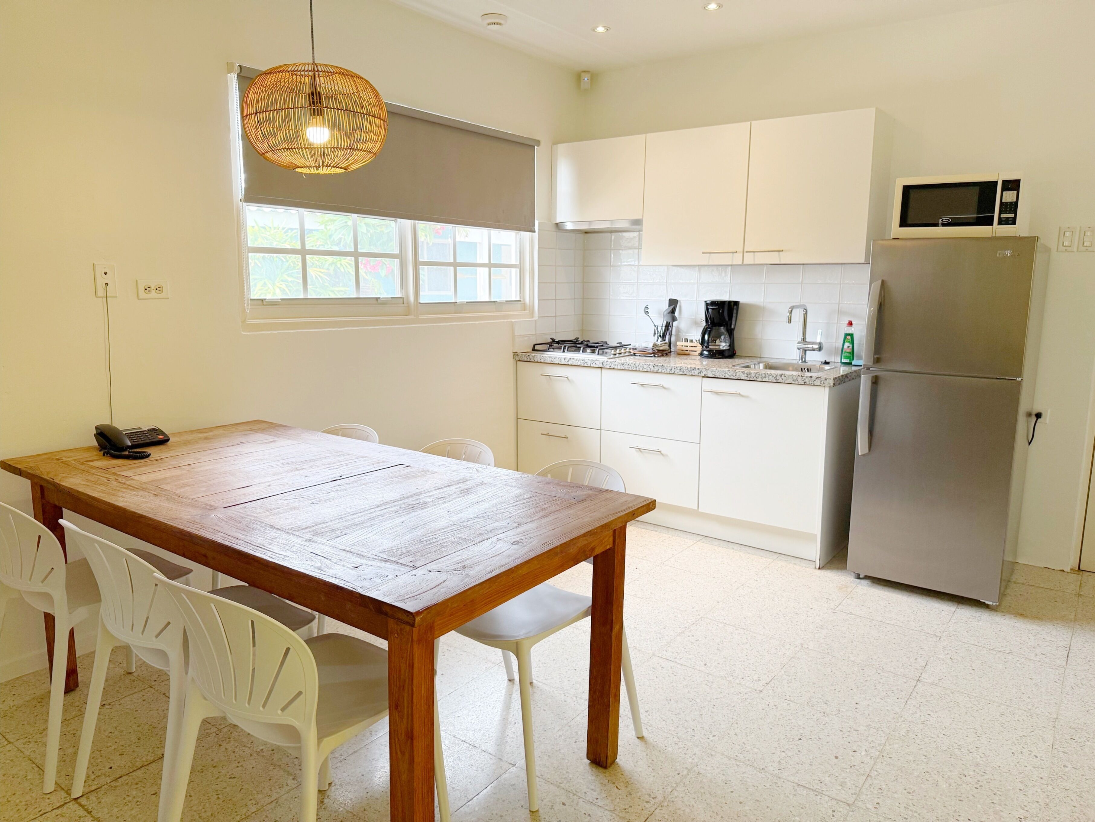 A modern kitchen with white cabinets, a stainless steel refrigerator, a microwave, and a wooden dining table with white chairs.