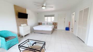 Um quarto espaçoso com uma cama, uma mesa de centro de vidro, uma cadeira de vime, um penteado e uma TV fixada na parede.