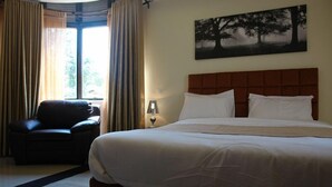 Een hotelkamer met een groot bed, een stoel, een lamp en een raam met gordijnen.