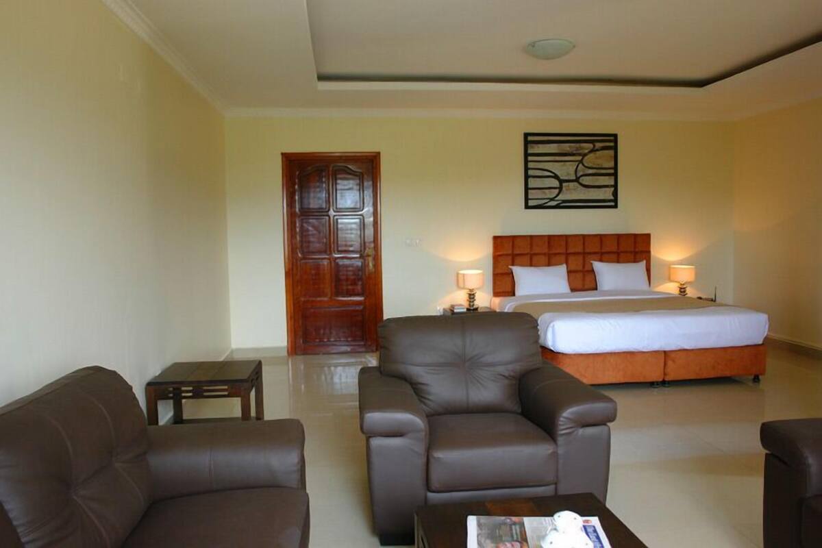 A hotel room with a large bed, two bedside lamps, a wooden door, a brown leather armchair, a small table, and a magazine on the table.