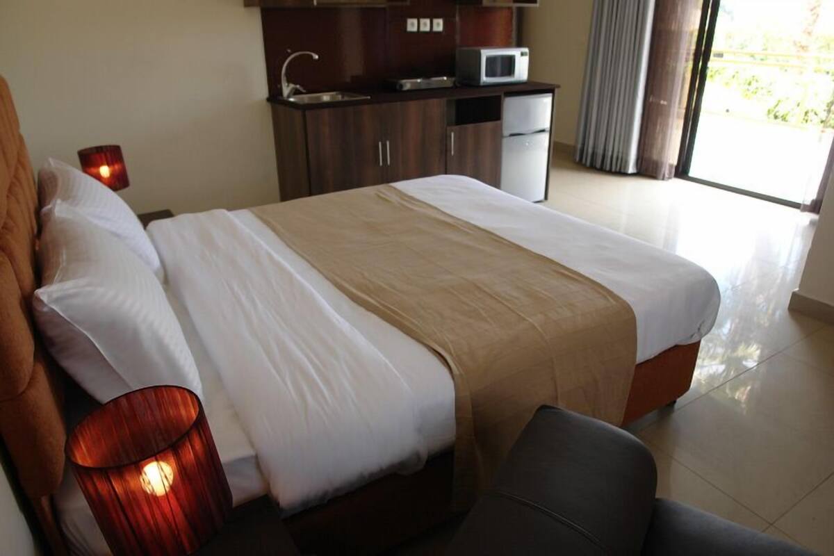 A hotel room with a bed, a desk, a microwave, and a window with curtains.
