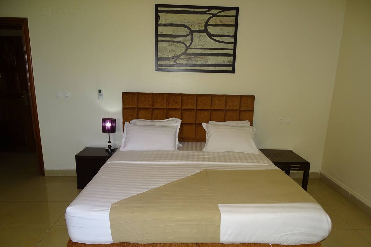 A neatly made bed with a wooden headboard, two bedside tables, and a wall-mounted abstract art piece.