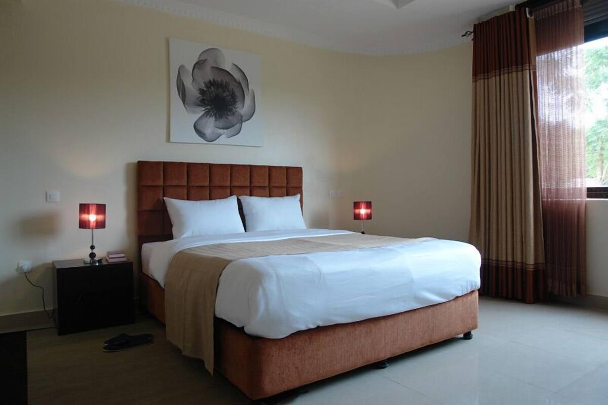 A neatly made bed with a wooden headboard, two bedside lamps, and a large abstract painting on the wall.