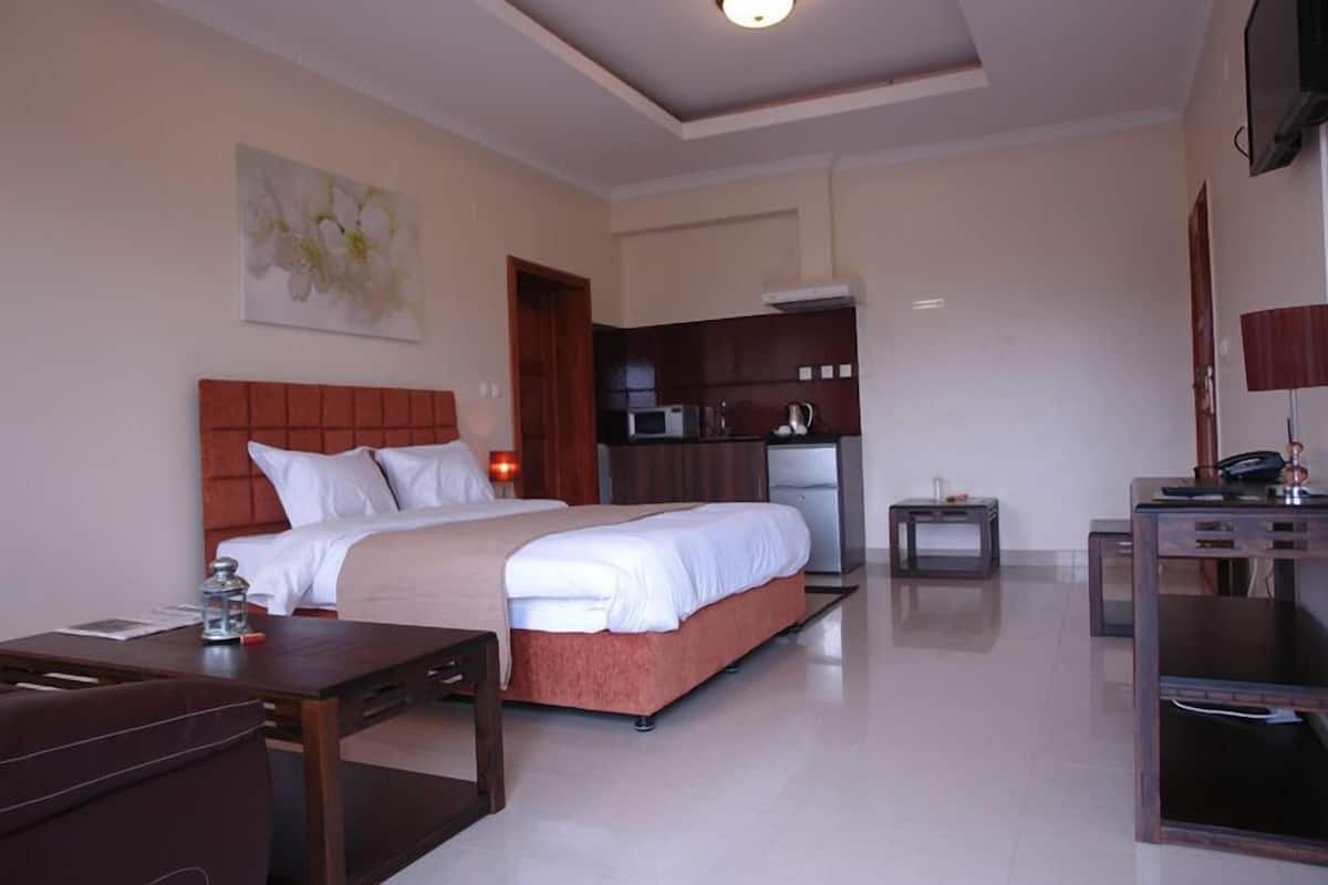 A hotel room with a large bed, a desk, a small kitchenette, and a TV.