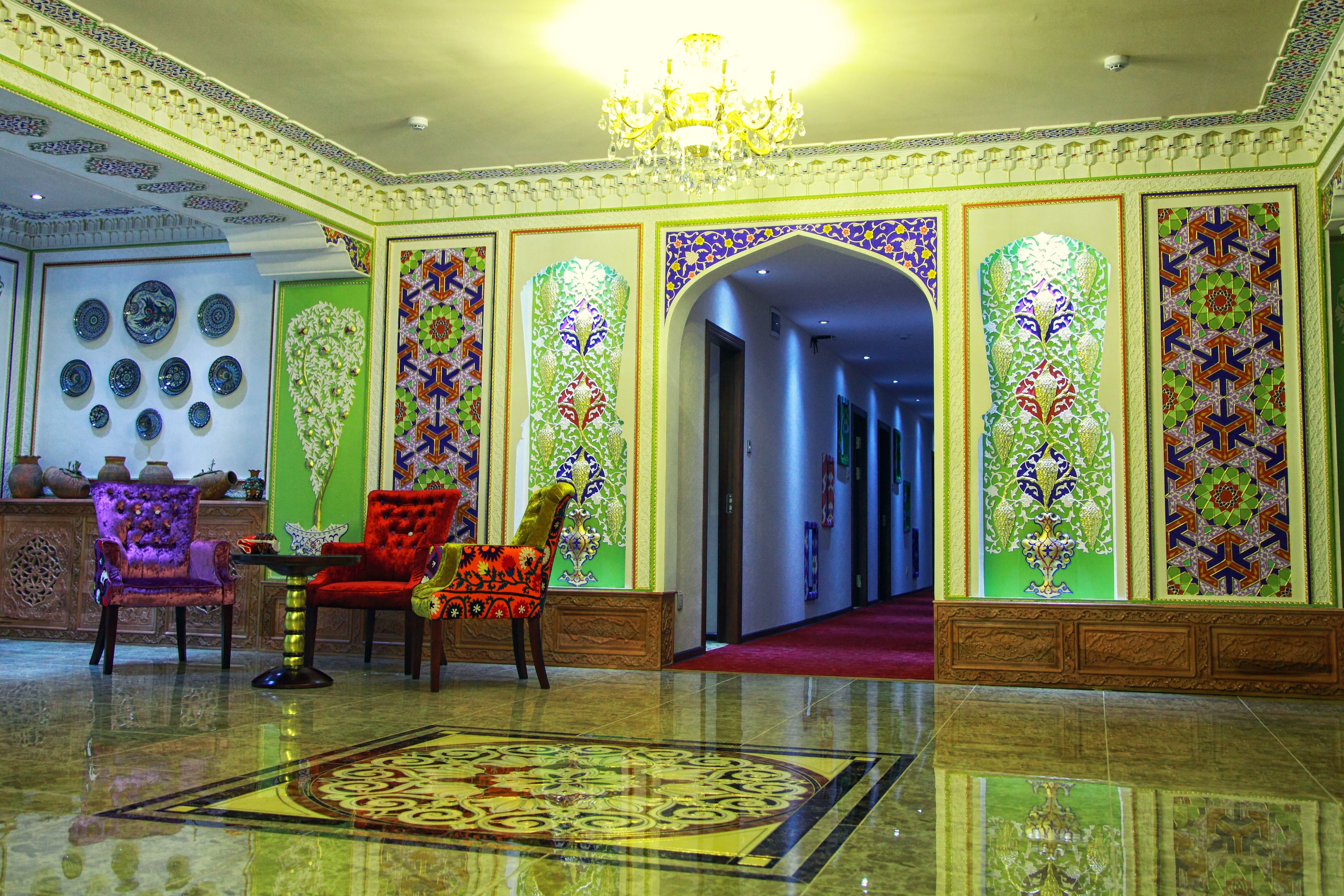 A luxurious lobby with ornate wall decorations, a chandelier, and a red carpeted area.