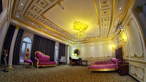 A luxurious hotel room with a large bed, a sitting area with a sofa and chairs, a desk, and a chandelier. - Emirhan (Samarkand)