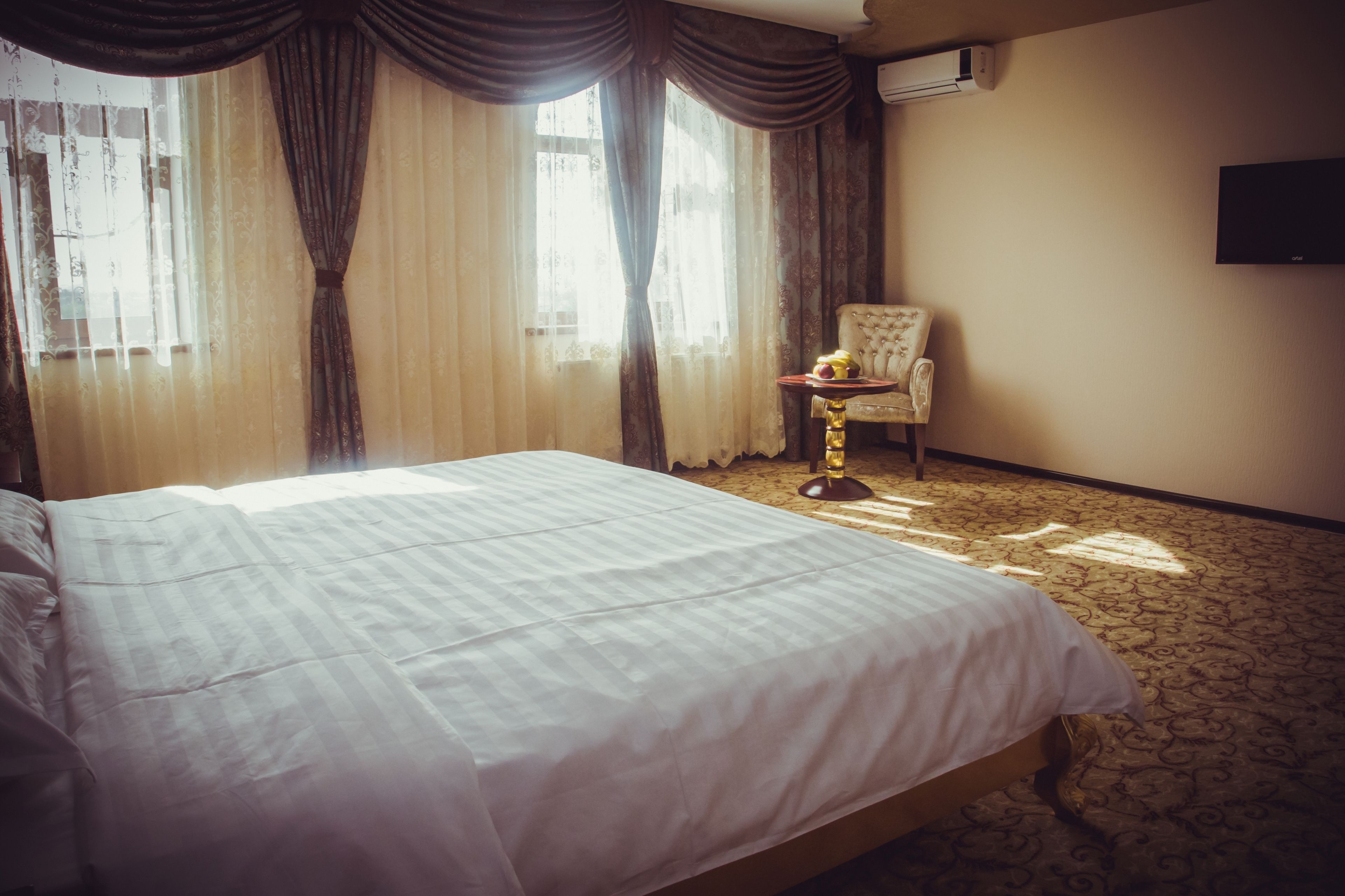 A hotel room with a large bed, a chair, a small table with a lamp, and a TV on the wall.