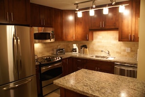 A kitchen with wooden cabinets, stainless steel appliances, granite countertops, and under-cabinet lighting.