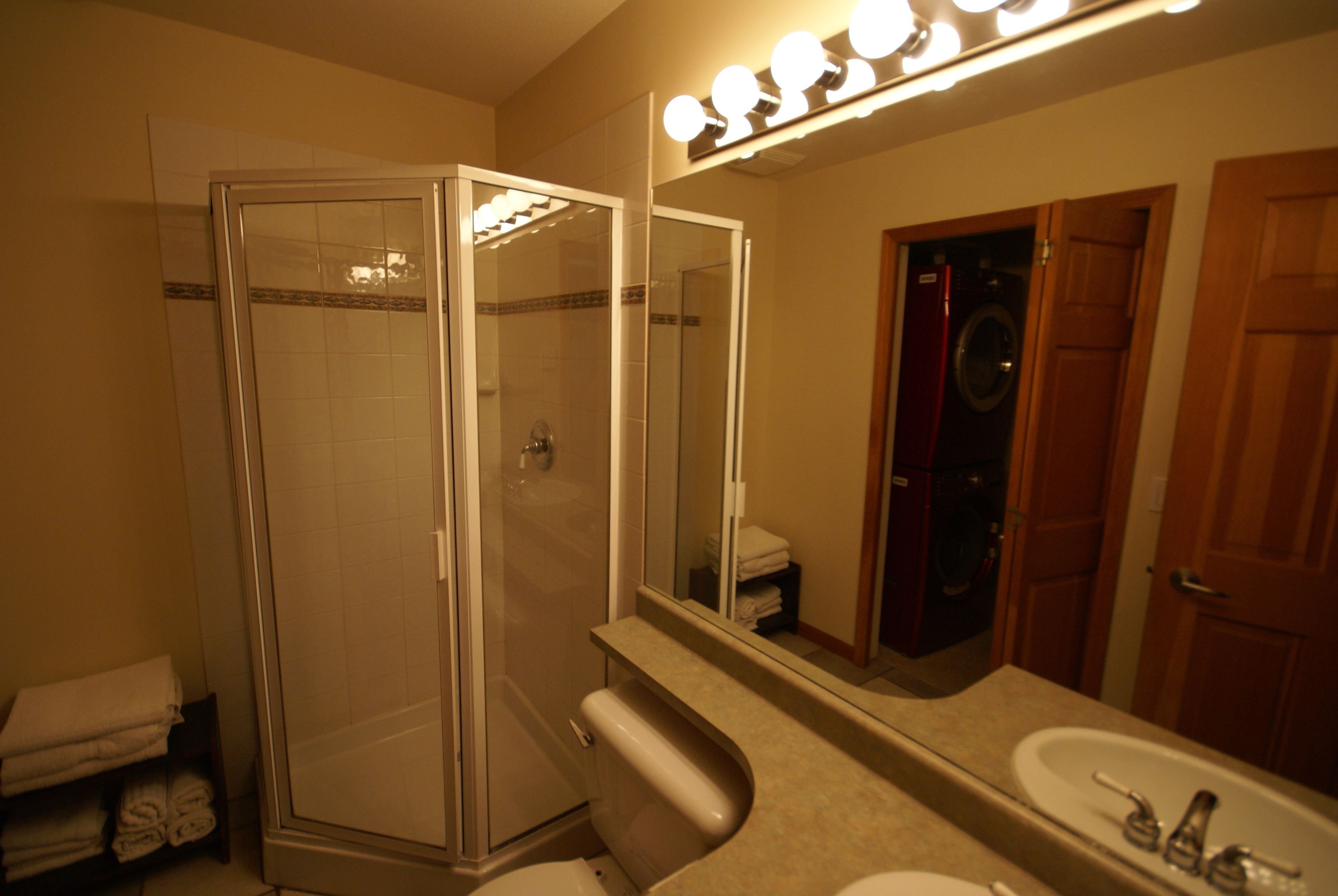 Une salle de bain avec une douche à parois de verre, un lavabo et un miroir avec des lumières au-dessus.