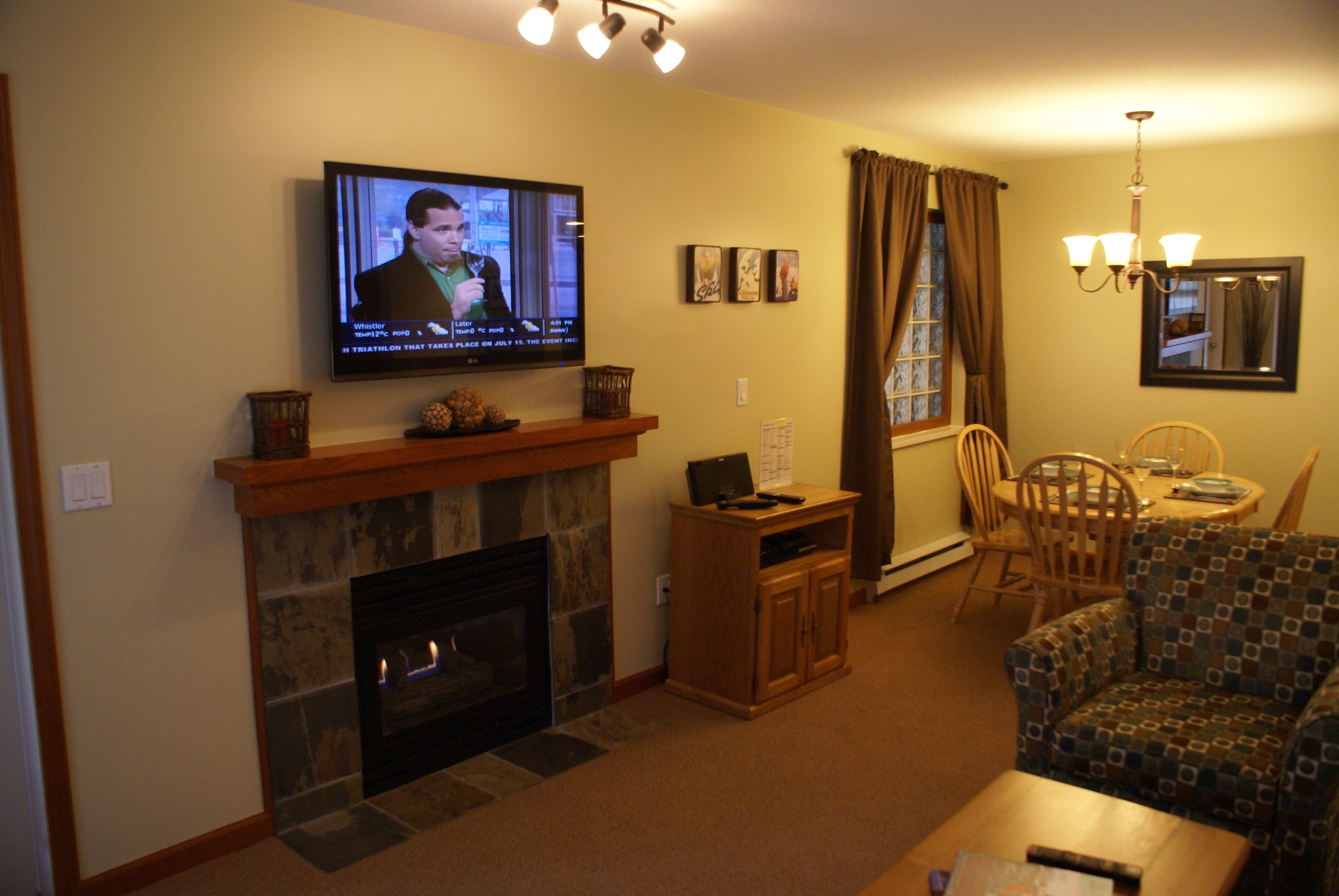 A living room with a fireplace, television, dining table, and patterned armchair.