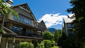 Ein zweistöckiges Gebäude mit einem Balkon im zweiten Stock, umgeben von Grünflächen und blauem Himmel.