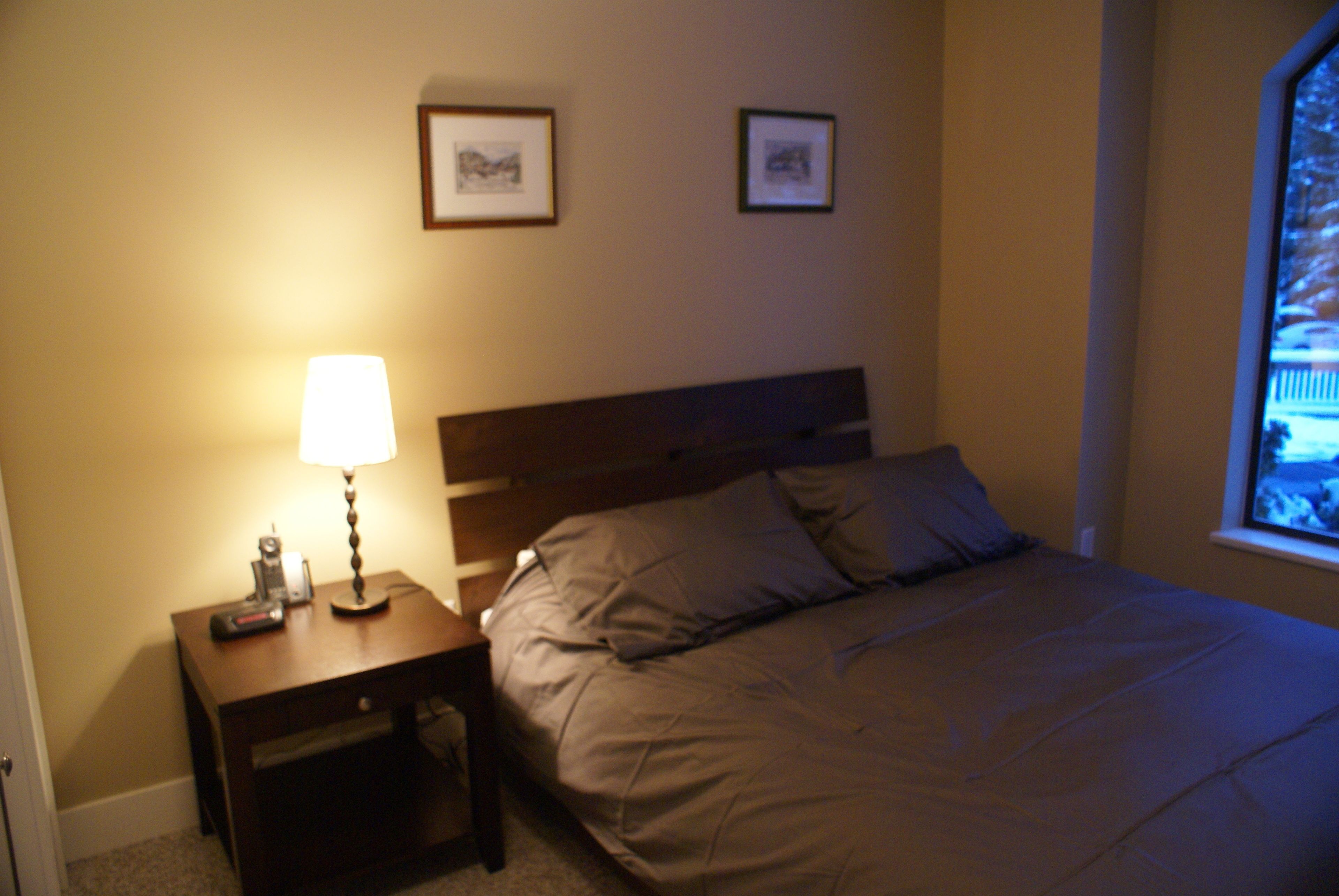 A bedroom with a bed, a nightstand with a lamp, and two framed pictures on the wall.
