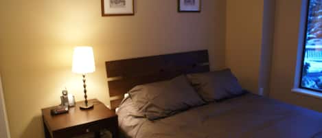 A bedroom with a bed, a nightstand with a lamp, and two framed pictures on the wall.