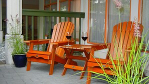 Eine Terrasse mit Holzkufen und einem Tisch, einem Blumentopf und einem Glas Rotwein.