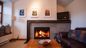Ein Wohnzimmer mit Kamin, einem Fernsehgerät auf einem Schrank und drei gerahmten Kunstwerken an der Wand.