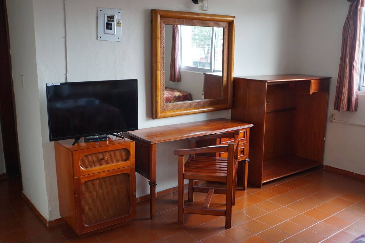 A room with a wooden desk, a television, a mirror, and a wardrobe.