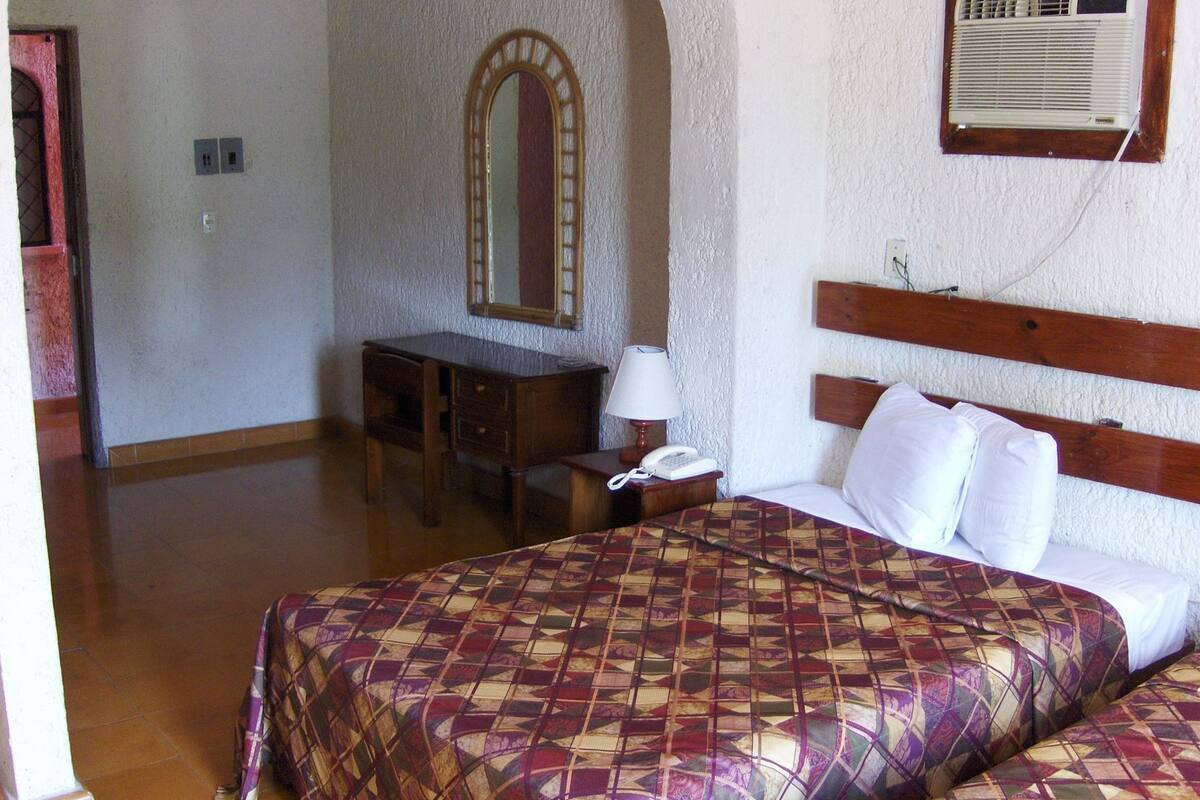 Una camera d'albergo con un letto, una scrivania, uno specchio, un telefono e un condizionatore d'aria.