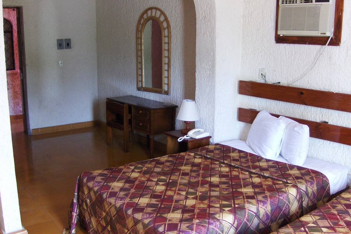 Una camera d'albergo con un letto, una scrivania, uno specchio e un condizionatore d'aria.