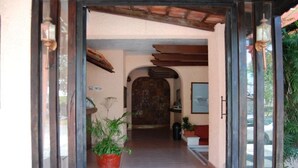 Uma entrada com piso de azulejos, porta de madeira e plantas em vasos.