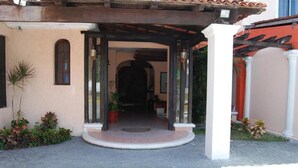 Uma entrada coberta com telhado ladrilhado, um pequeno jardim e um caminho que leva a um edifício.