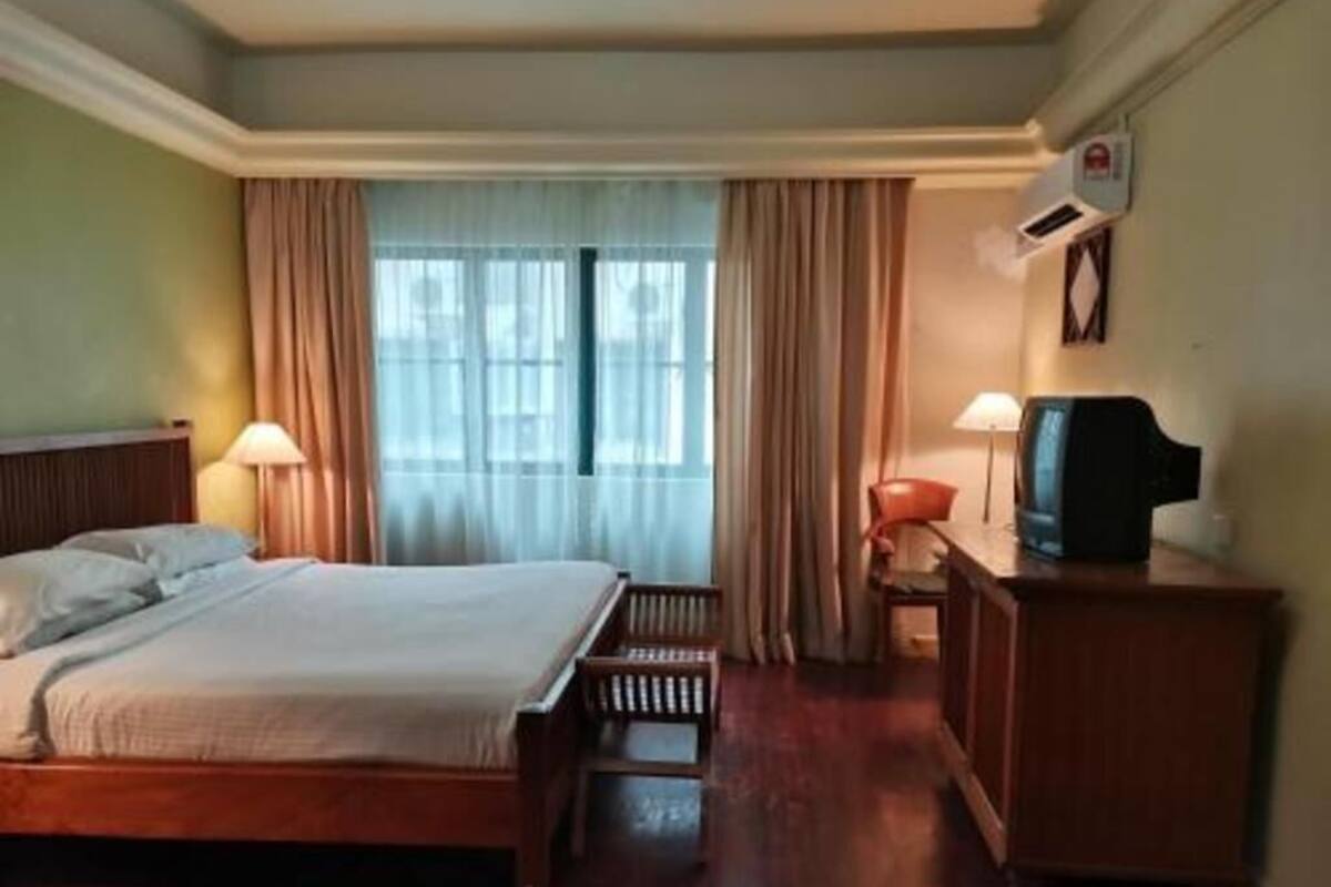 A hotel room with a bed, a desk with a television, a lamp, and a window with curtains.