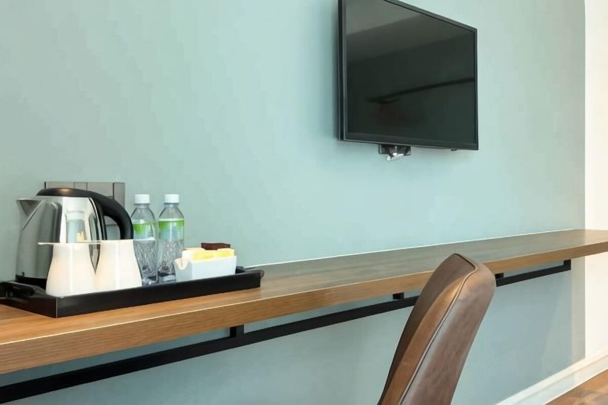 A hotel room with a flat-screen TV mounted on the wall, a wooden desk with a tray of amenities, and a chair.