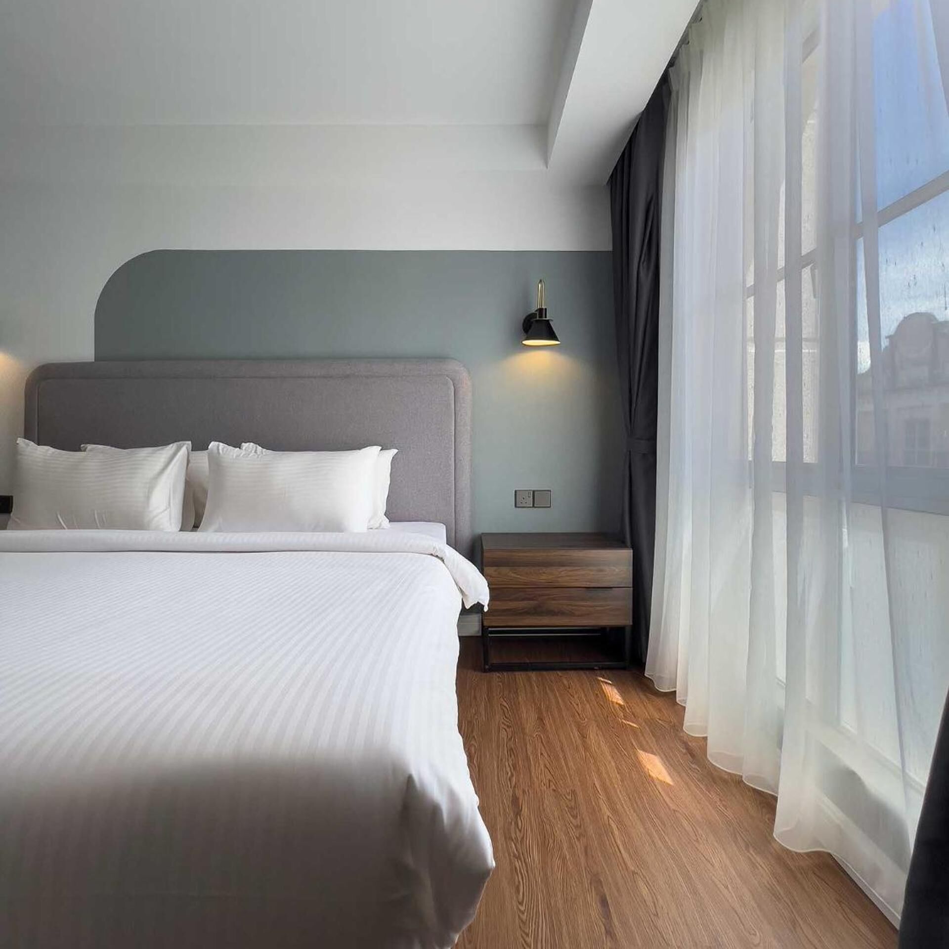 Een moderne hotelkamer met een groot bed, een nachtkastje, een wandlamp en dunne gordijnen.