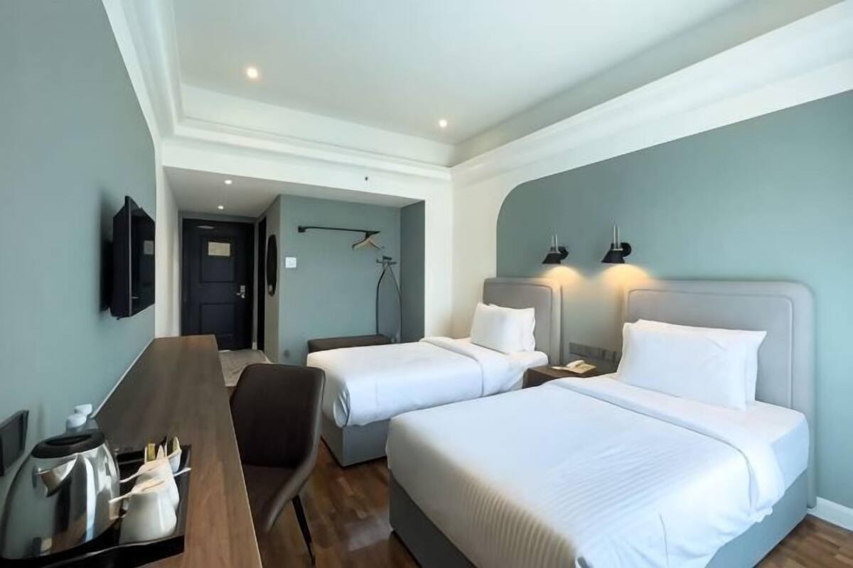 A hotel room with two beds, a desk, a chair, a TV, and a door leading to another room.