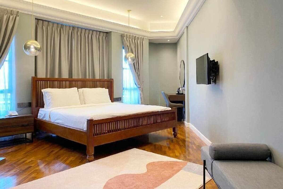 A modern hotel room with a wooden bed, a desk, and a grey sofa.