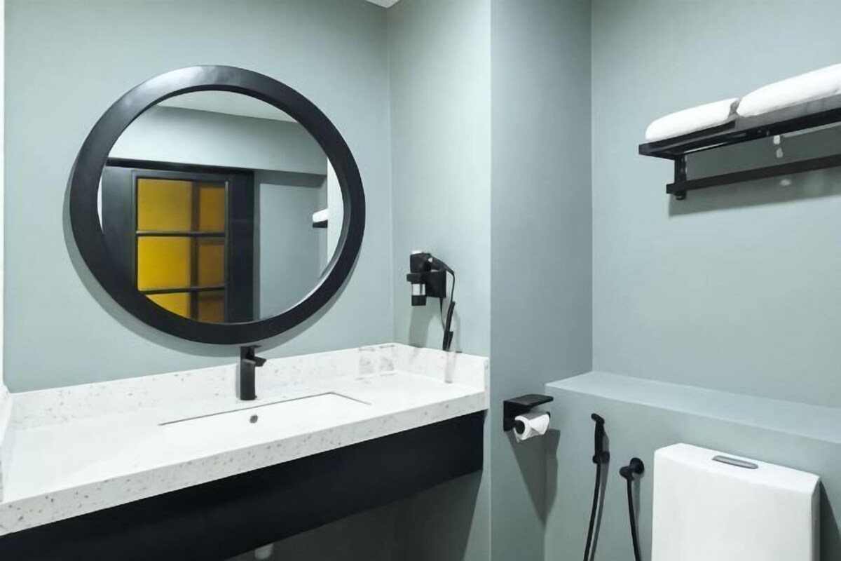 A bathroom with a round mirror, a white sink, a towel rack, and a toilet paper holder.