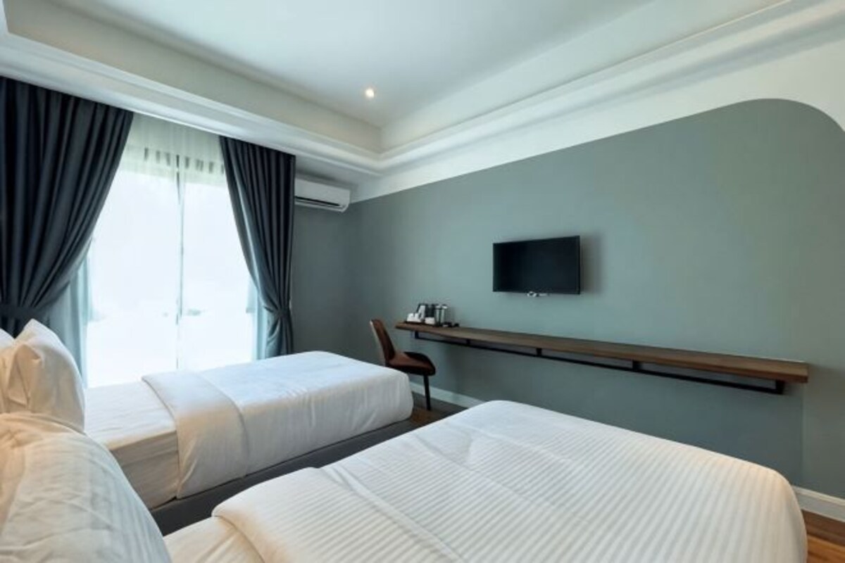 Habitación de hotel con dos camas, un televisor montado en la pared y un escritorio con una silla.