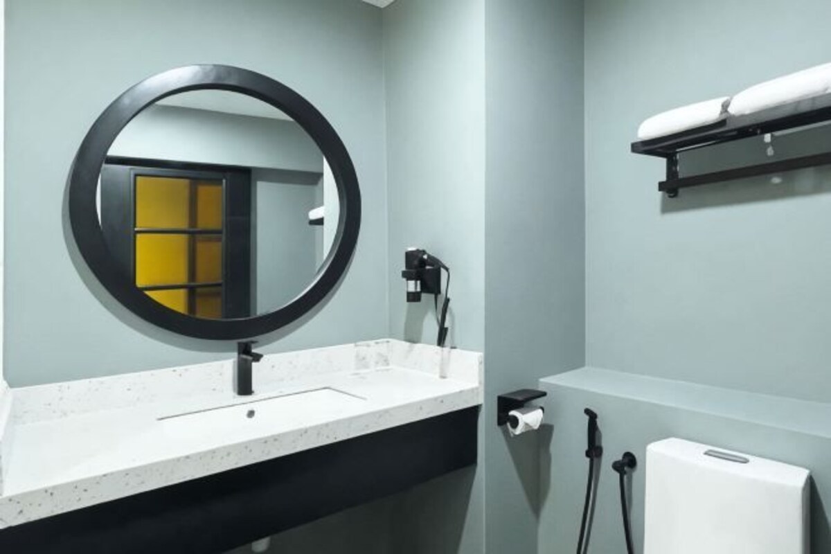 Un baño con un espejo redondo, un lavabo blanco, un perchero para toallas y un dispensador de papel higiénico.