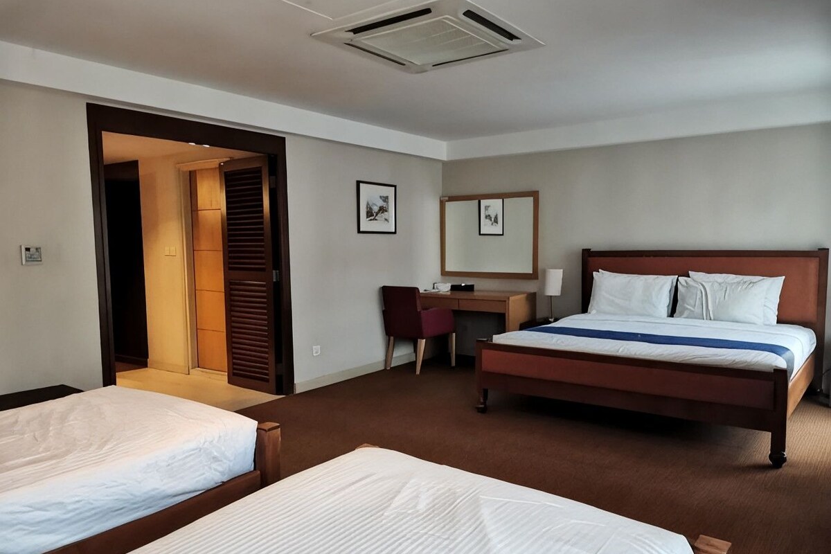 Quarto de hotel com duas camas, uma escrivaninha, uma cadeira e um espelho.