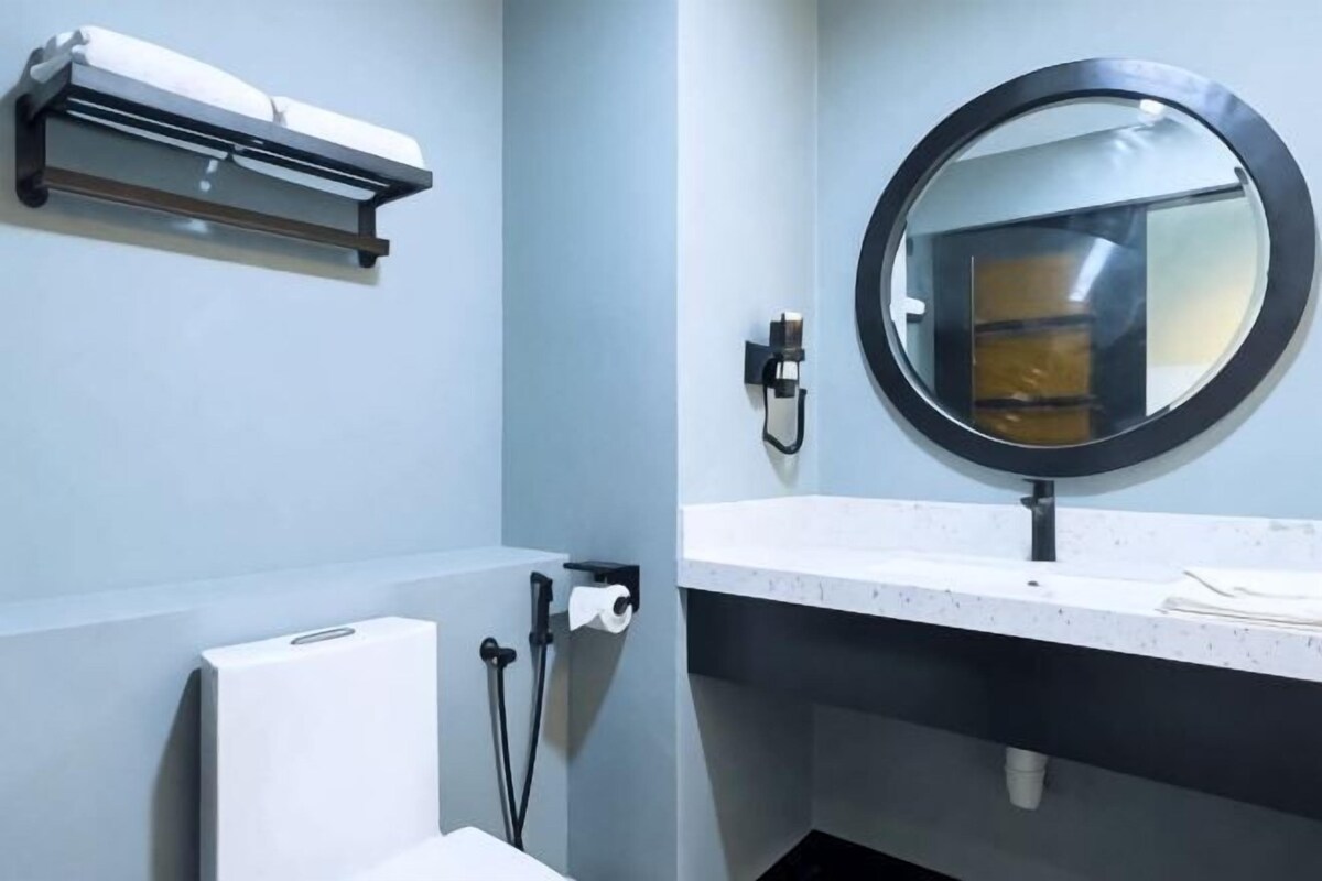 A bathroom with a toilet, a sink, a mirror, a towel dispenser, and a towel rack.