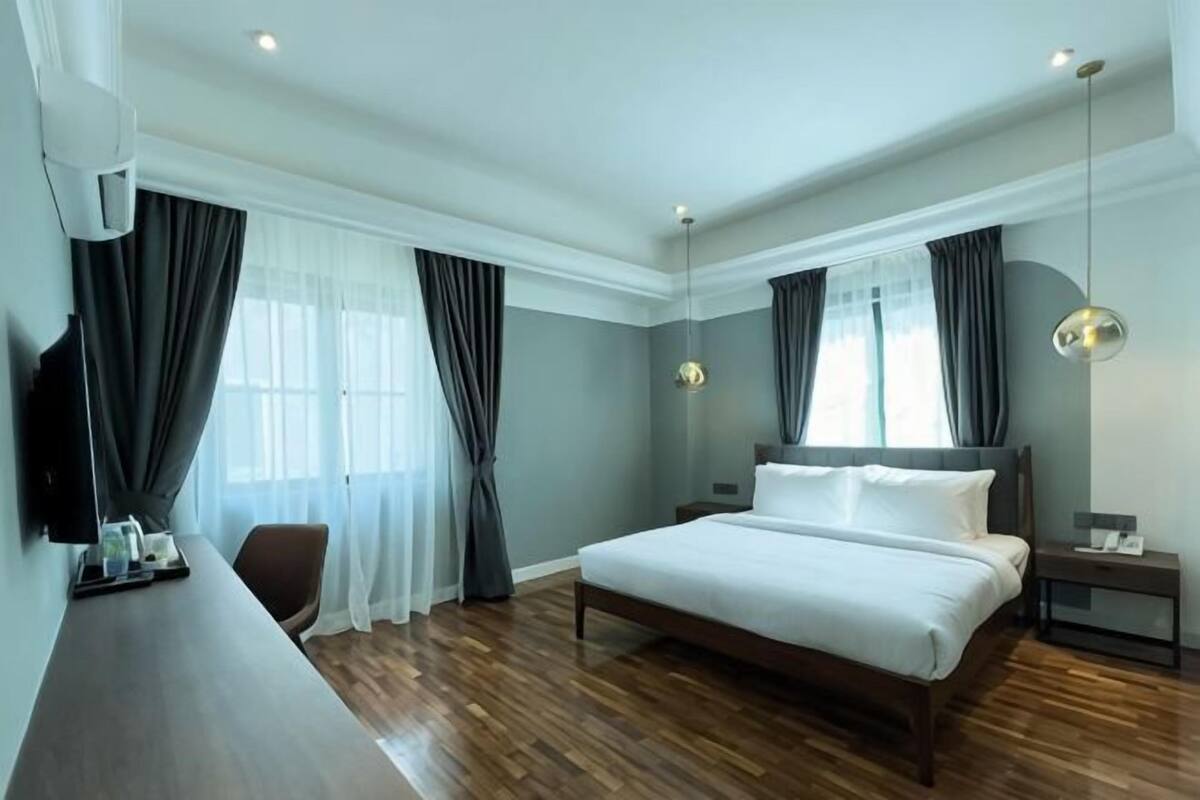 A hotel room with a large bed, a desk, a chair, a TV, and a window with curtains.