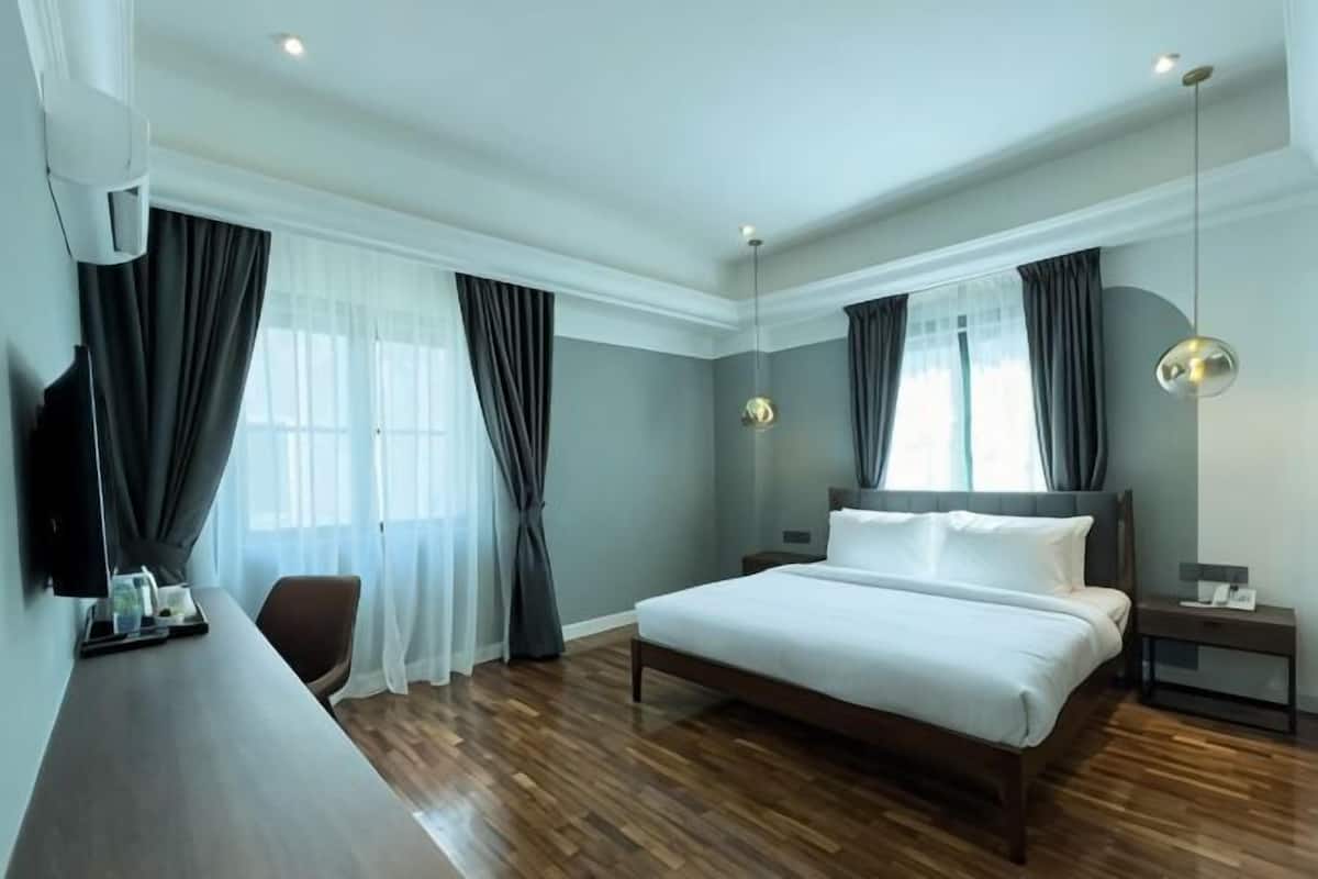 A hotel room with a large bed, a desk, a chair, a TV, and a window with curtains.